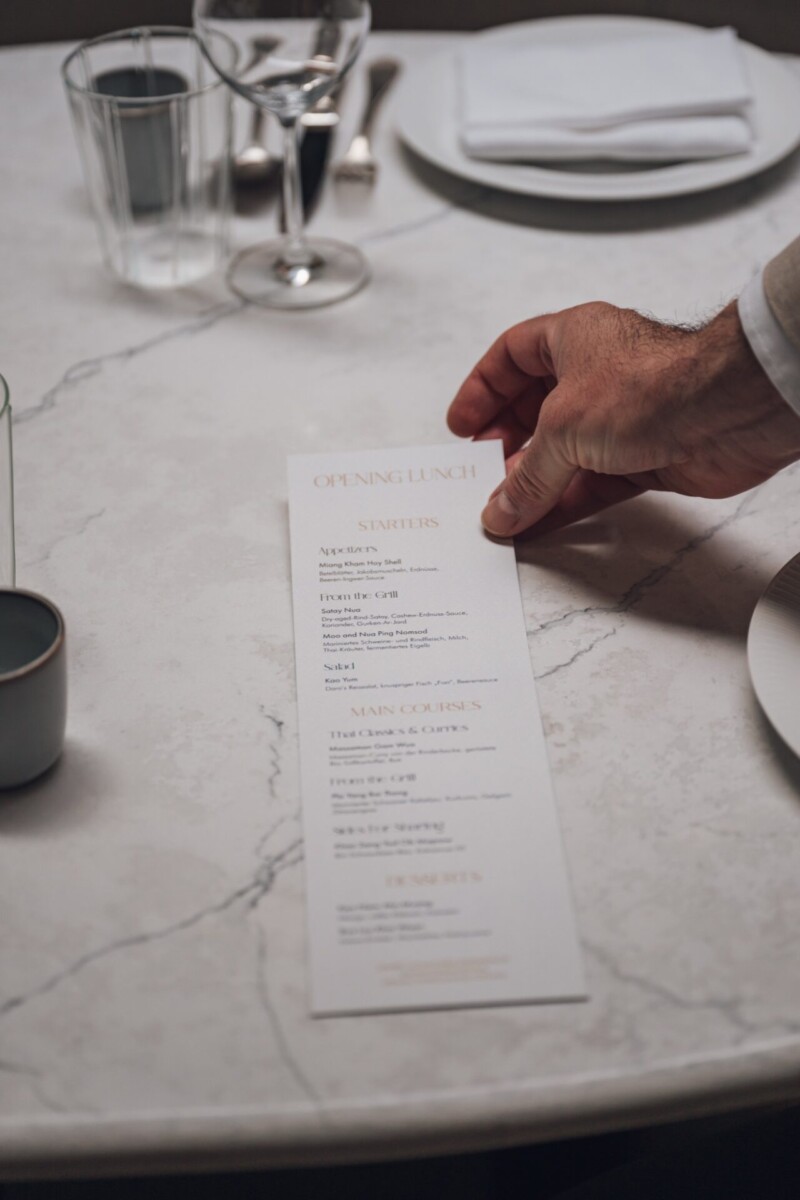 Gedruckte Menükarte des DARA Cuisine Eröffnungslunch auf einem Marmortisch