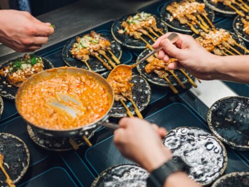 Satay-Spieße und Beilagen werden an einem Tisch serviert